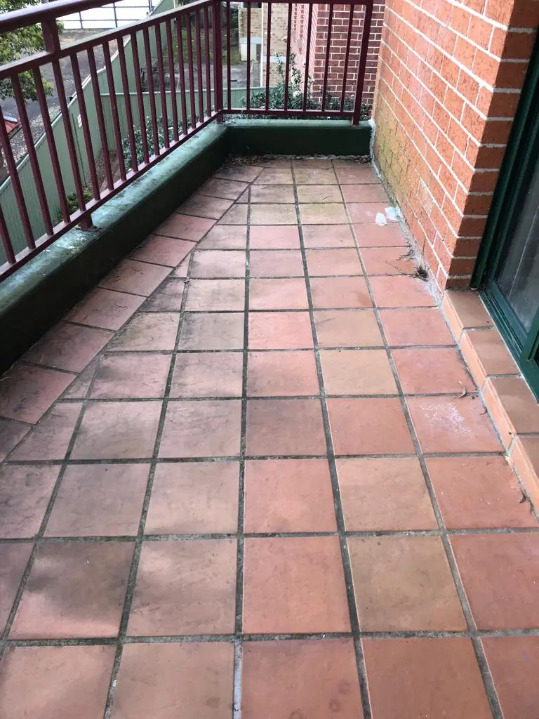 Before: terracotta balcony with green upstands and dark, dirty grout.