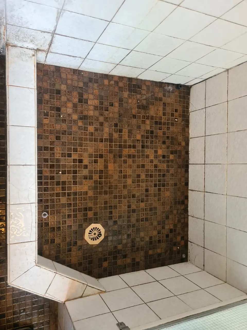 Before: brown mosaic shower floor with stained grout.